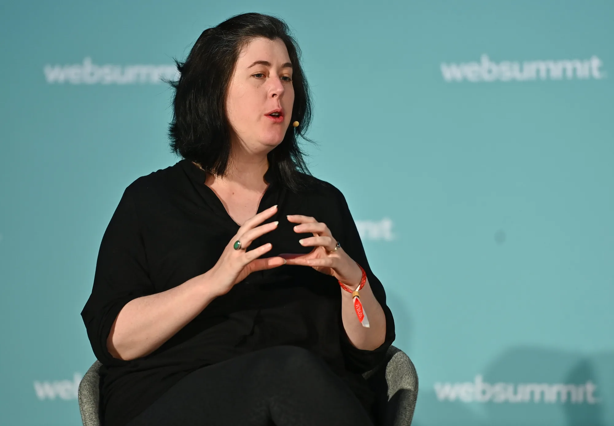 Hazel Savage seated on a conference stage mid-sentence, hands raised as she explains something, against a pale blue Web Summit backdrop.