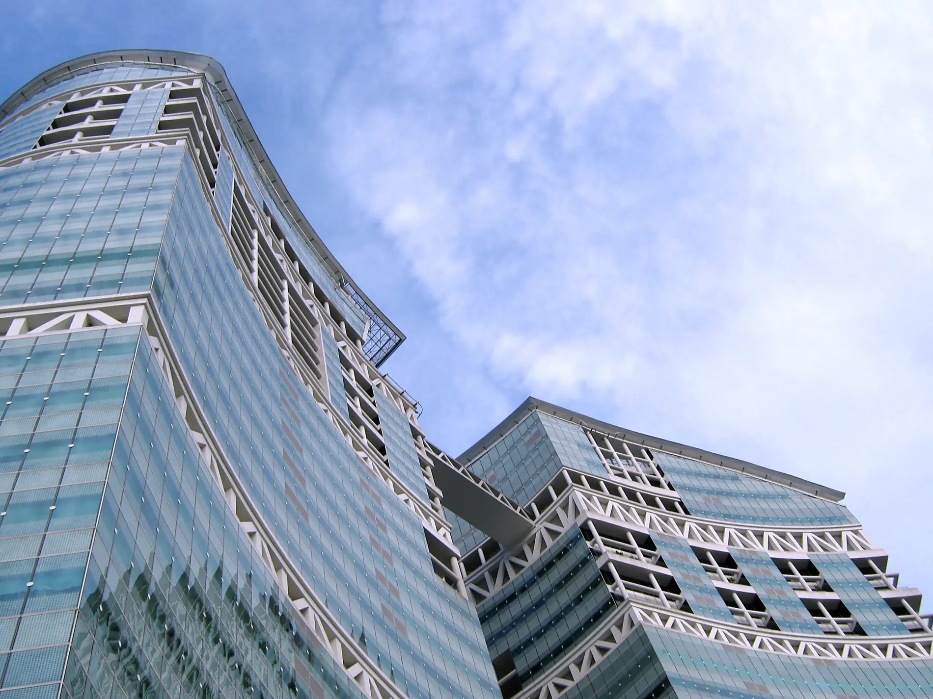 Looking up at the curved blue-green glass towers of Fusionopolis at one-north, Singapore, against a bright sky.