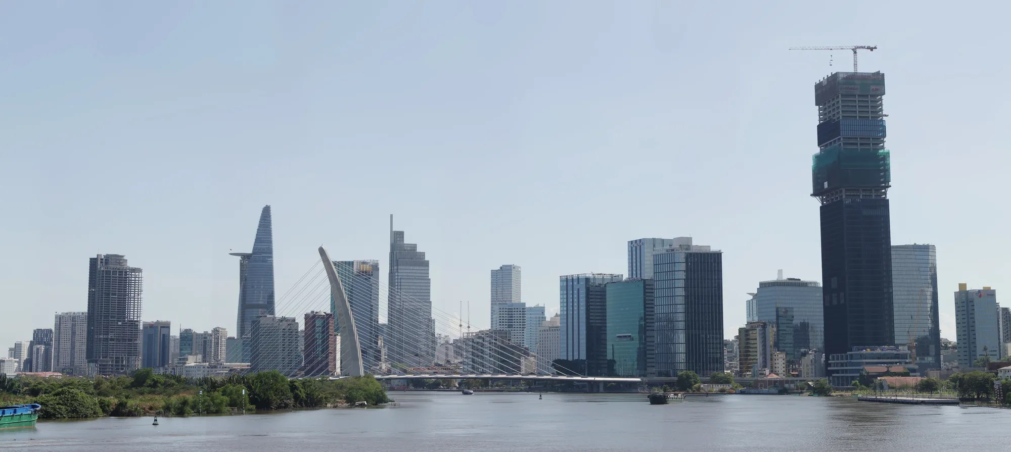 Ho Chi Minh City seen across the Saigon River: the district one skyline, a cable-stayed bridge, and a tower under construction at the right.